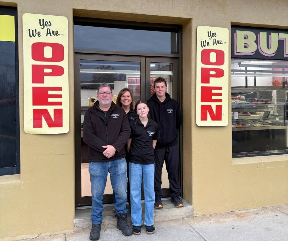 Paul Horton and his family, owners of Locky’s Countryside Meats, standing outside their butcher shop at 514 Macauley Street, Albury NSW. Two large vertical signs on either side of the door read “Yes We Are… OPEN” in red letters.
